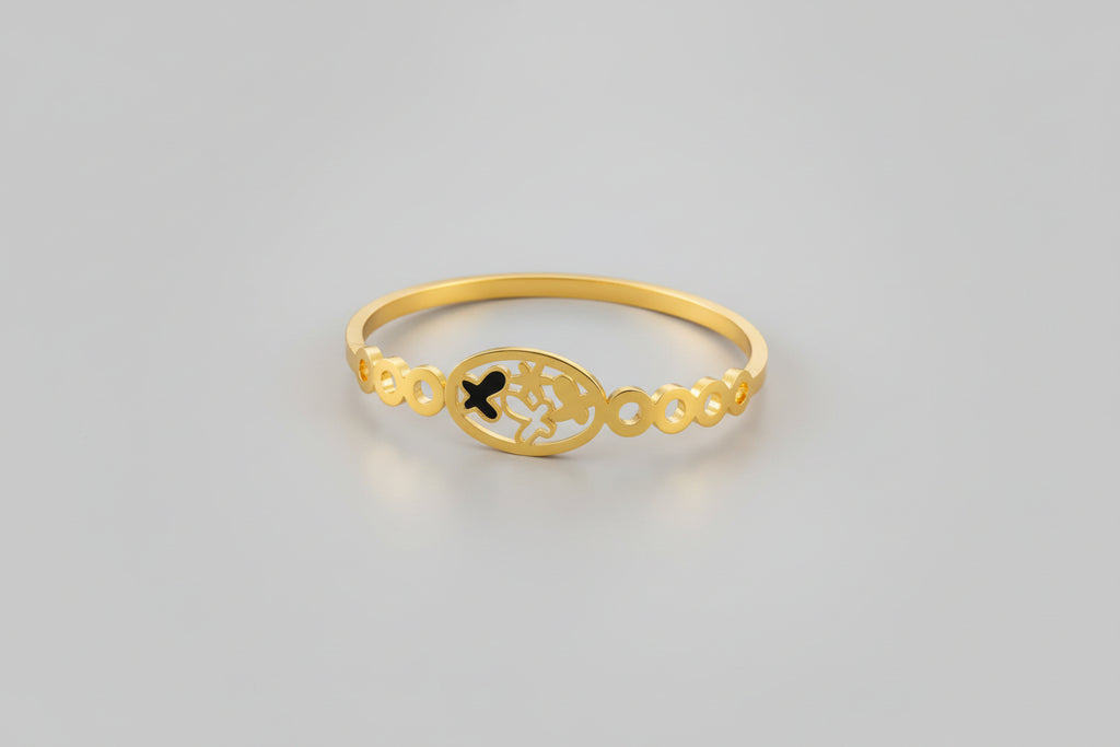 A dainty gold-toned open-cuff bangle featuring a central multi-petaled floral motif and two smaller four-leaf clover charms on either side, displayed on a vibrant pink background.