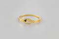A dainty gold-toned open-cuff bangle featuring a central multi-petaled floral motif and two smaller four-leaf clover charms on either side, displayed on a vibrant pink background.