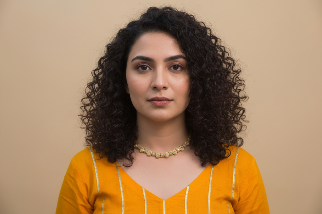 A delicate gold-toned necklace set featuring alternating square and circular stations with intricate textured patterns and small pastel-colored stones. The set includes matching drop earrings with a similar motif, worn by a person in a bright yellow outfit.