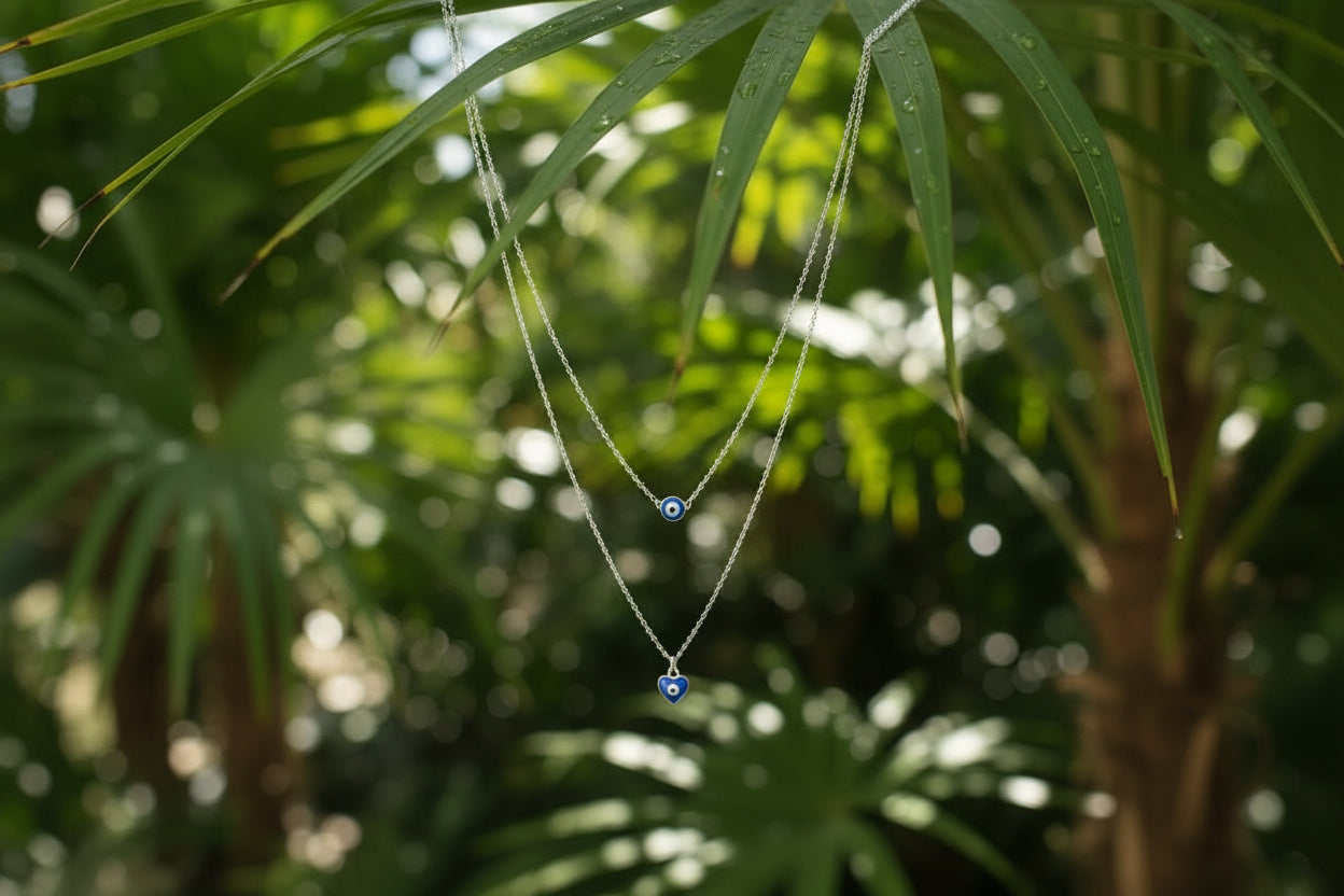 Double-layered silver chain necklace with a round evil eye bead and a heart-shaped evil eye pendant