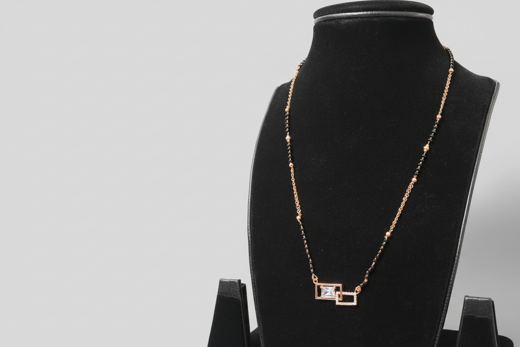 A contemporary mangalsutra featuring a unique dual-strand chain of black beads and gold links. The pendant consists of two interlocking rectangular frames—one gold-toned and one set with clear crystals—housing a central emerald-cut clear stone, displayed on a black jewelry bust.