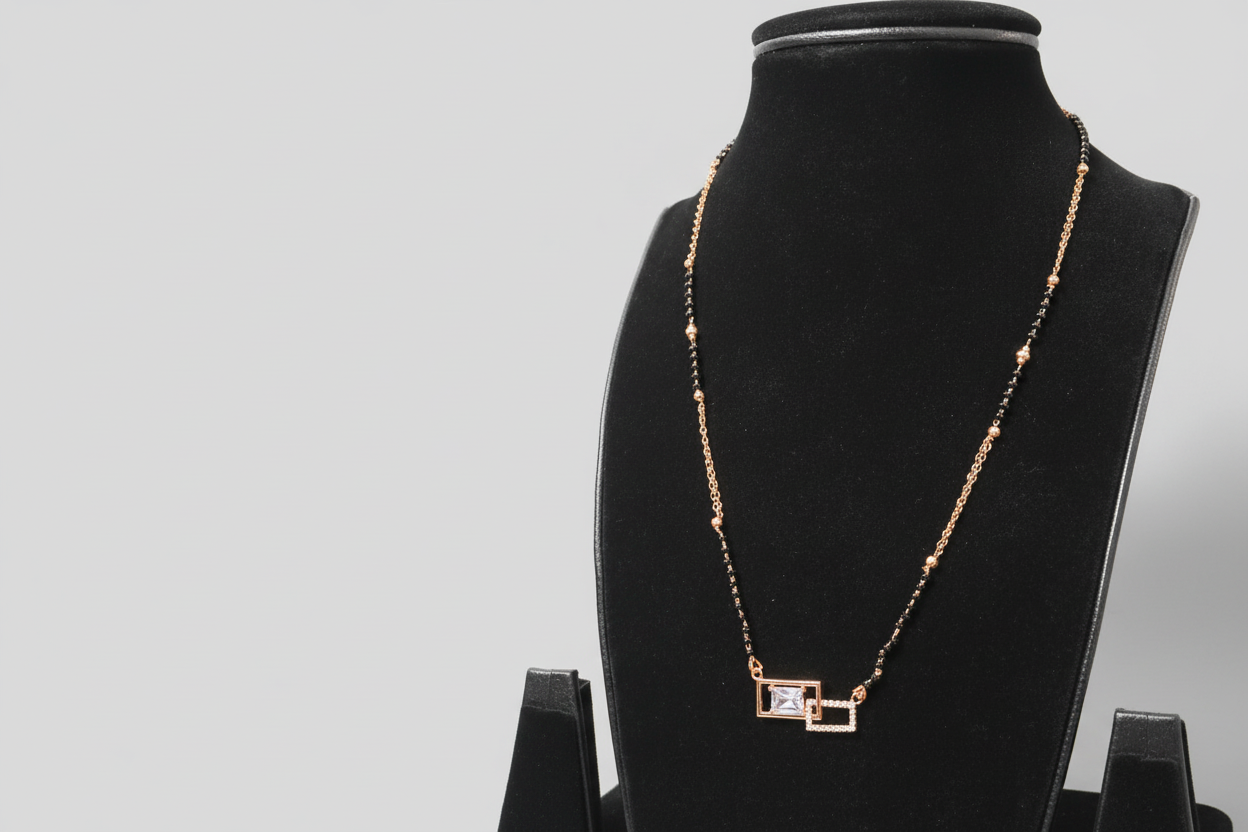 A contemporary mangalsutra featuring a unique dual-strand chain of black beads and gold links. The pendant consists of two interlocking rectangular frames—one gold-toned and one set with clear crystals—housing a central emerald-cut clear stone, displayed on a black jewelry bust.