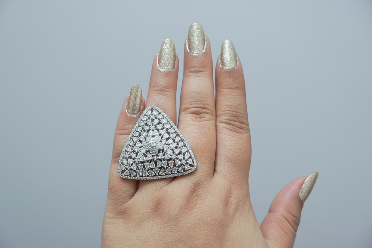 Triangular silver ring with gemstones on a hand against a dark background