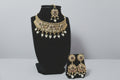 A heavy, traditional antique gold-finished choker necklace and matching maang tikka set. The design features intricate floral and circular metalwork, accented with green, pink, and clear stones, and finished with multiple white pearl droplets, displayed on a black jewelry bust.