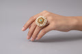 Traditional gold-finish cocktail ring featuring a central green emerald-style stone surrounded by a lush border of white faux pearls and intricate gold filigree work.