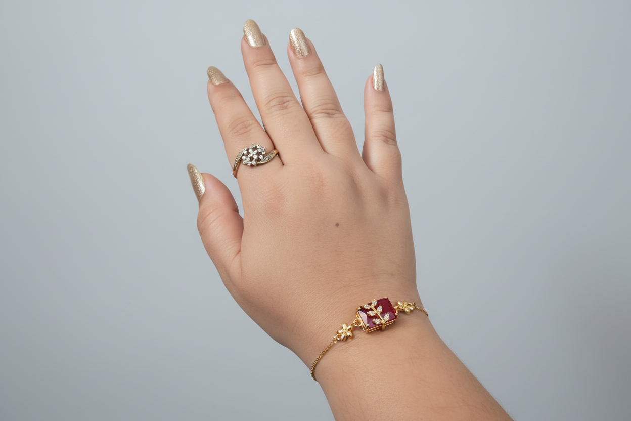 A dainty gold-toned chain bracelet featuring a central rectangular ruby-red stone. A small, gold leaf-shaped motif encrusted with tiny clear crystals is set atop the red stone, worn on a wrist against a vibrant purple background.