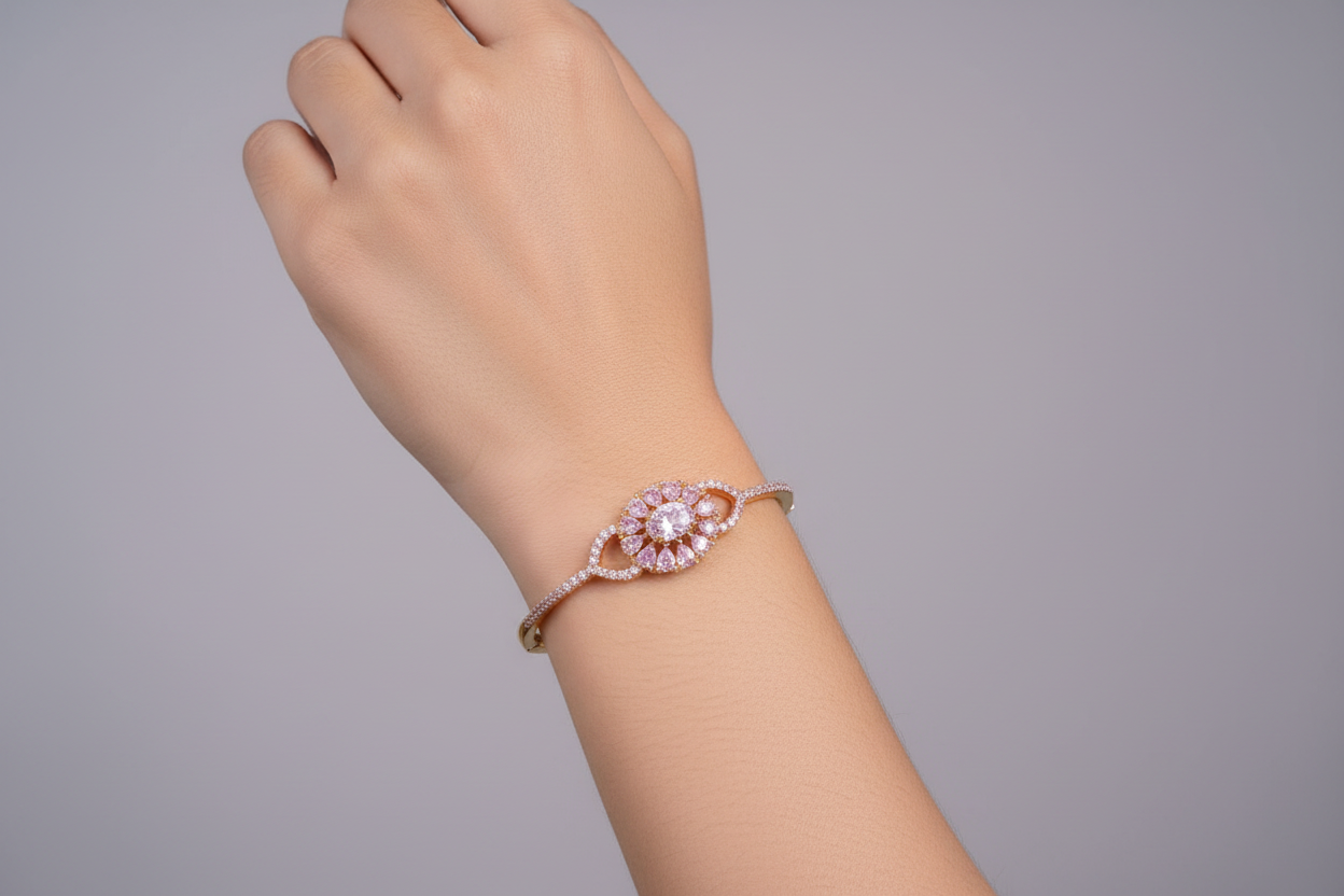 A delicate gold-tone bangle featuring a prominent central floral motif made of sparkling clear stones, with a slim band partially encrusted with smaller crystals, displayed on a dark green velvet surface.