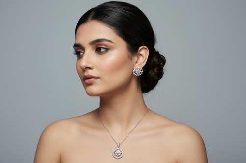 A three-piece jewelry set in a silver-tone finish, featuring a circular pendant and two matching stud earrings. Each piece is intricately set with clear shimmering crystals in a floral or snowflake-like pattern, displayed against a dark black background.