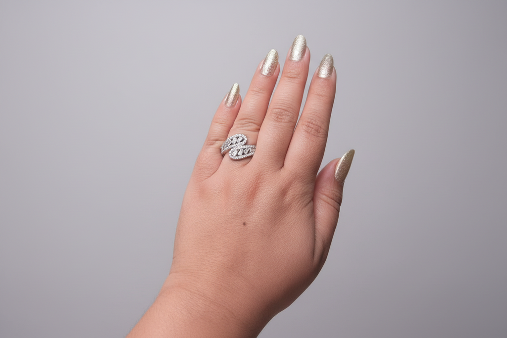 Modern silver-finish ring featuring a unique S-curve design encrusted with baguette and round-cut white crystals, displayed on a hand against a natural green leaf background.