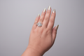 Modern silver-finish ring featuring a unique S-curve design encrusted with baguette and round-cut white crystals, displayed on a hand against a natural green leaf background.