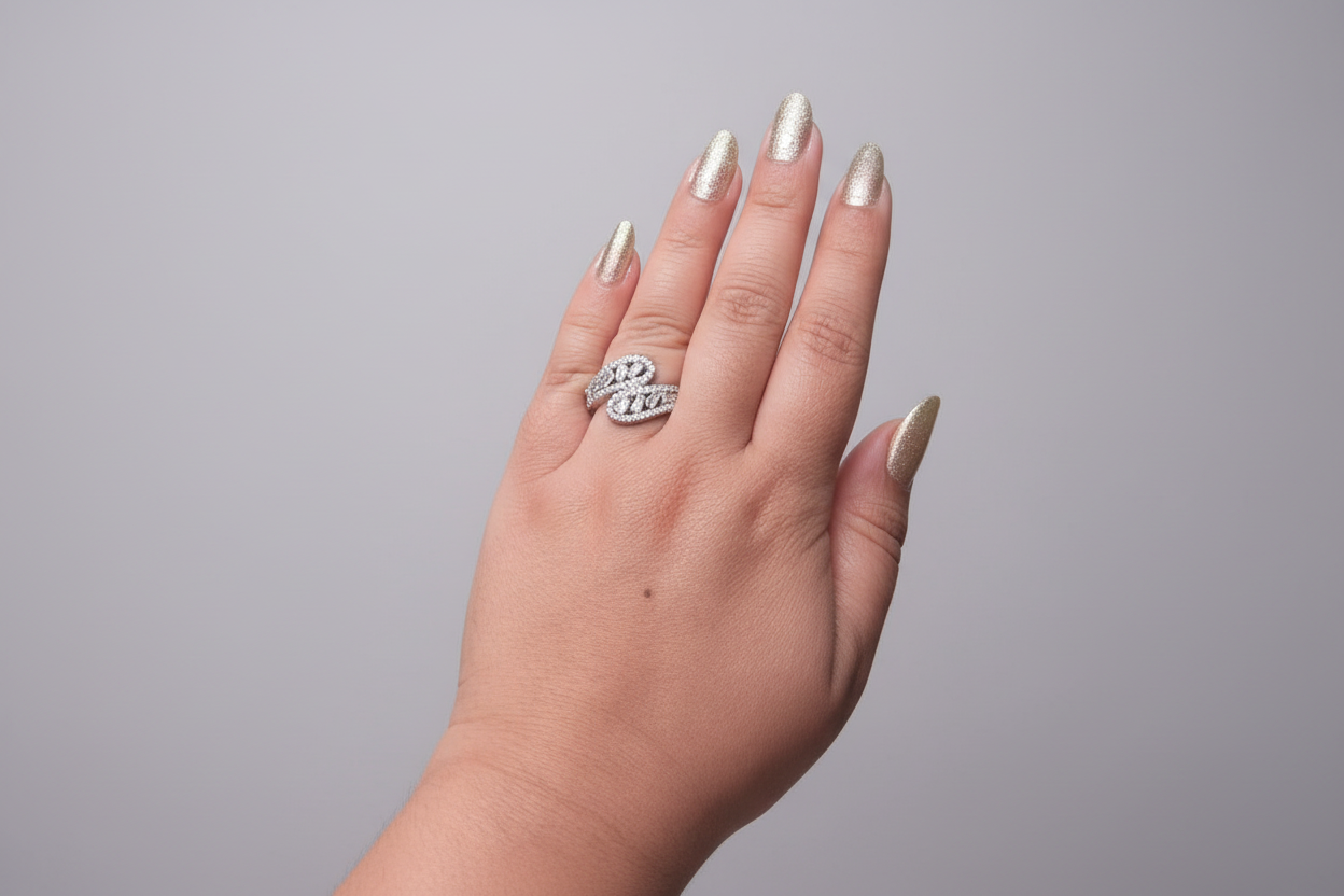 Modern silver-finish ring featuring a unique S-curve design encrusted with baguette and round-cut white crystals, displayed on a hand against a natural green leaf background.
