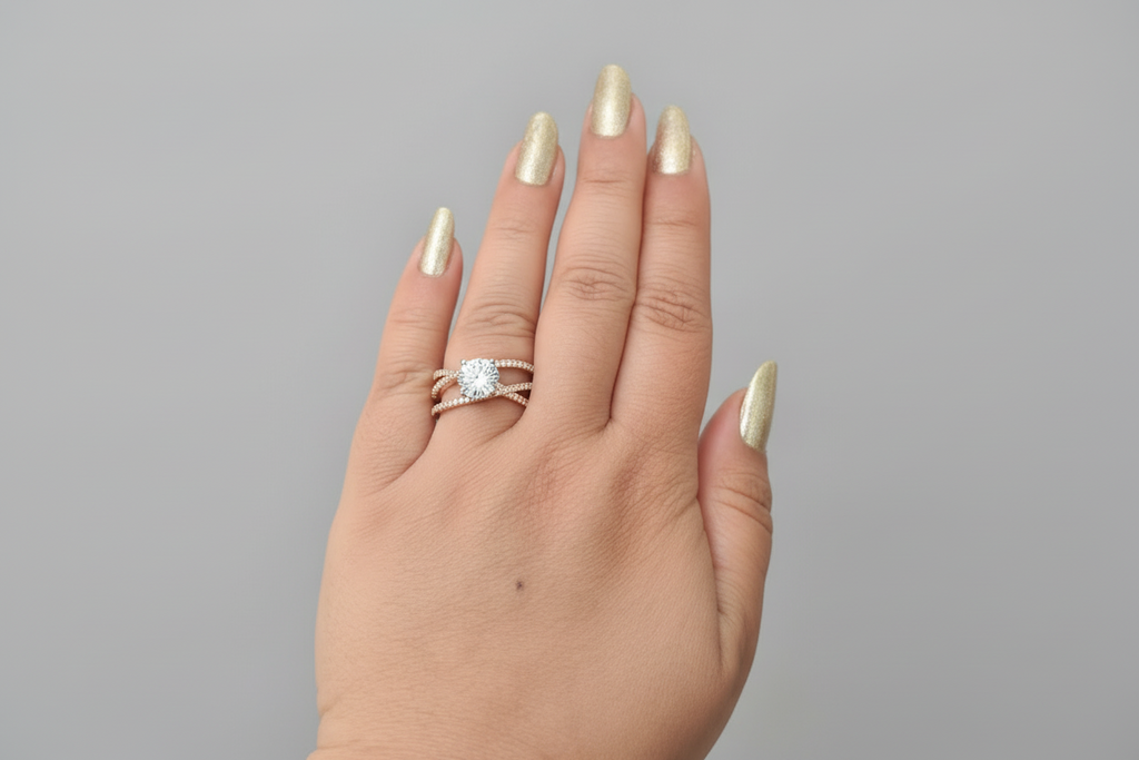 Modern silver-finish criss-cross ring featuring interlocking pavé crystal bands and a brilliant central solitaire stone, displayed on a hand with gold manicured nails.