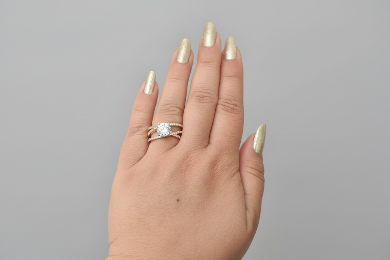 Modern silver-finish criss-cross ring featuring interlocking pavé crystal bands and a brilliant central solitaire stone, displayed on a hand with gold manicured nails.