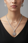 Elegant silver-finish jewelry set featuring a circular lattice-work pendant and matching drop earrings encrusted with white crystals, displayed on a black velvet bust.