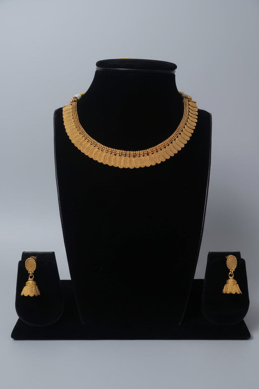 A traditional antique gold-toned necklace set featuring a wide collar-style choker with repeating scalloped textured stations. The set includes matching Jhumka-style drop earrings with a similar granular pattern