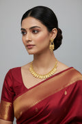 A traditional gold-toned jewelry set featuring a necklace with a row of scalloped, shield-shaped stations with intricate textured detailing. The set includes matching drop earrings with a similar motif and hanging gold accents, displayed against a black velvet background