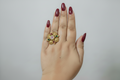 Hand wearing a gold ring with colorful gemstones against a pink textured background