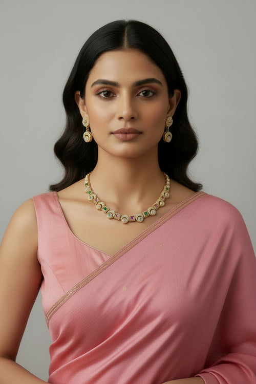 A delicate gold-toned necklace set featuring alternating square and circular stations with intricate textured patterns and small pastel-colored stones. The set includes matching drop earrings with a similar motif, worn by a person in a bright yellow outfit.
