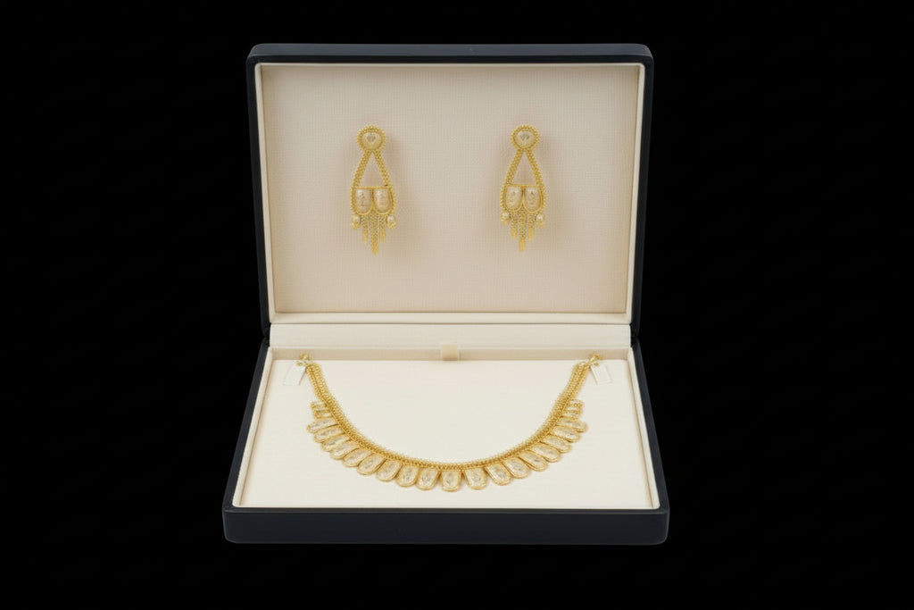 A traditional gold-toned jewelry set featuring a necklace with a row of scalloped, shield-shaped stations with intricate textured detailing. The set includes matching drop earrings with a similar motif and hanging gold accents, displayed against a black velvet background