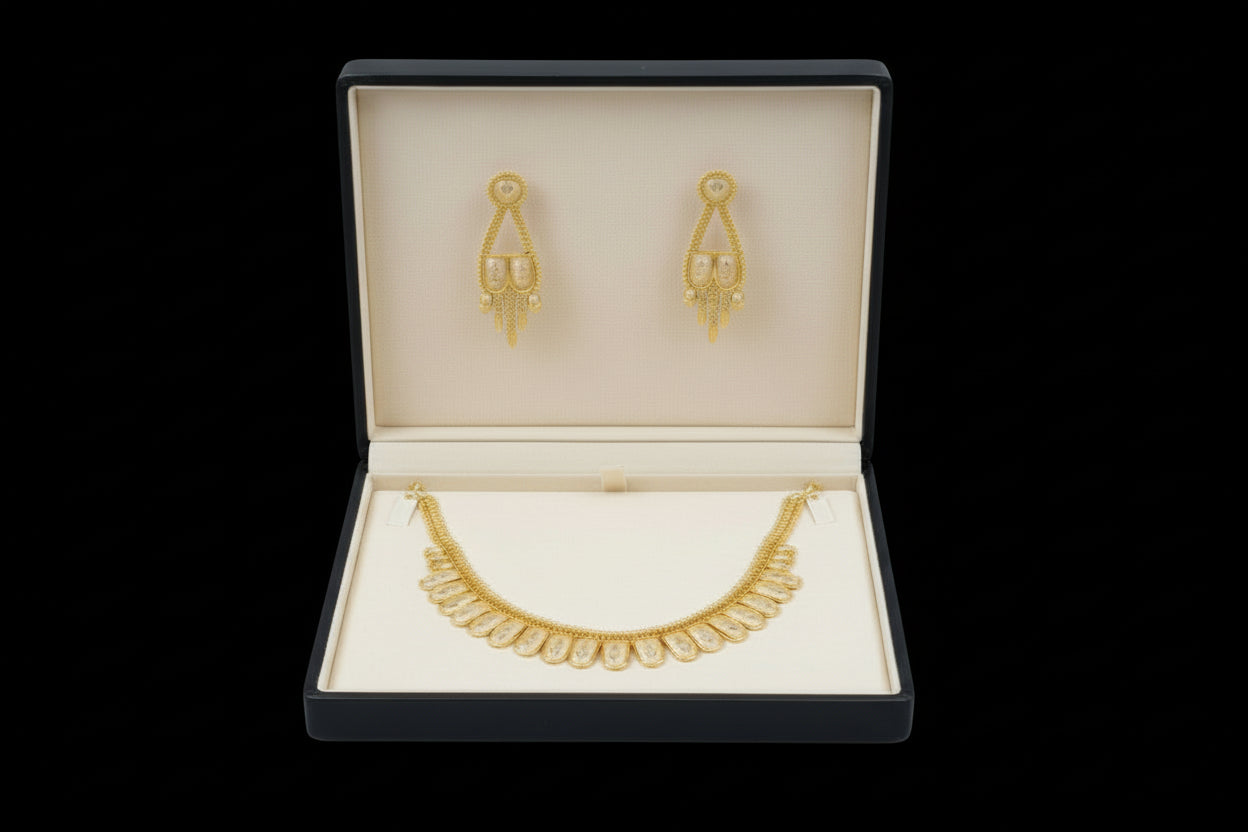 A traditional gold-toned jewelry set featuring a necklace with a row of scalloped, shield-shaped stations with intricate textured detailing. The set includes matching drop earrings with a similar motif and hanging gold accents, displayed against a black velvet background
