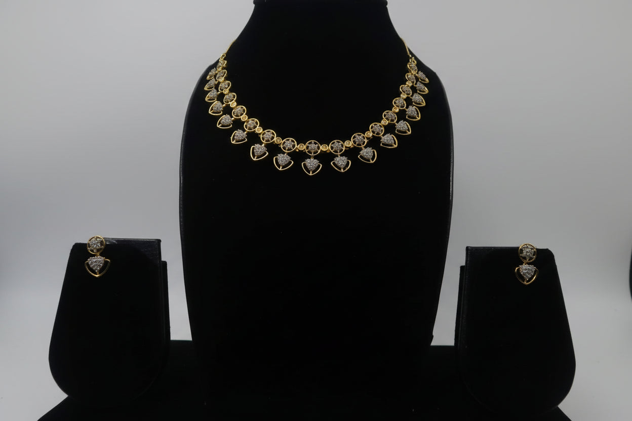 A stunning gold-toned necklace set featuring a continuous row of heart-shaped or spade-shaped stations. Each station is set with a star-patterned cluster of clear crystals. The set includes matching small stud earrings and is displayed on a black jewelry bust
